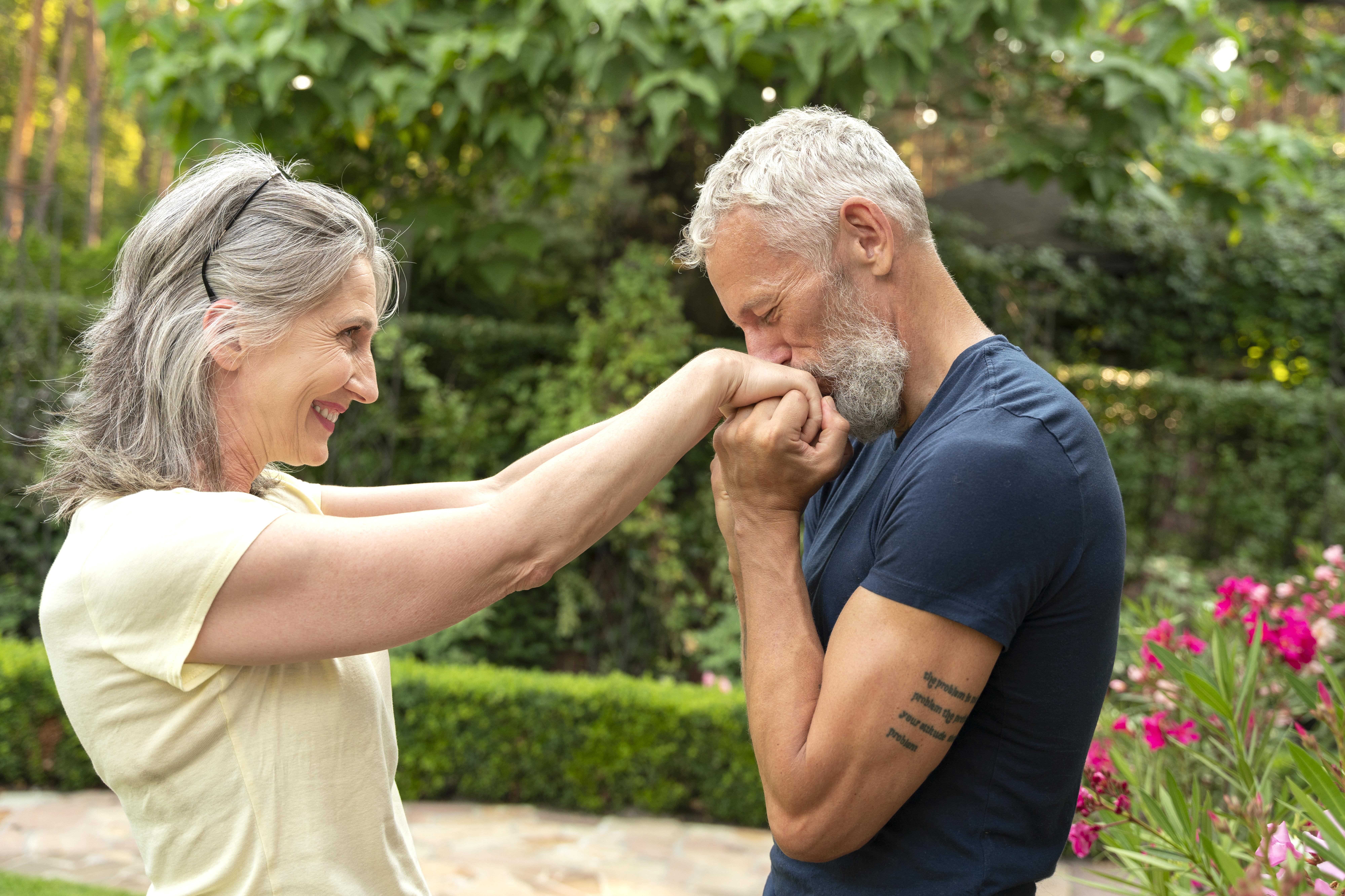 a senior man kissing his wife’s hands while they walk outdoors a senior man kissing his wife's hands while they walk outdoors